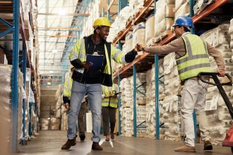men-fist-bump-teamwork-warehouse-logistics-clipboard-greeting-by-shelf-respect-inspection-people-happy-inventory-distribution-smile-supply-chain-industrial-plant
